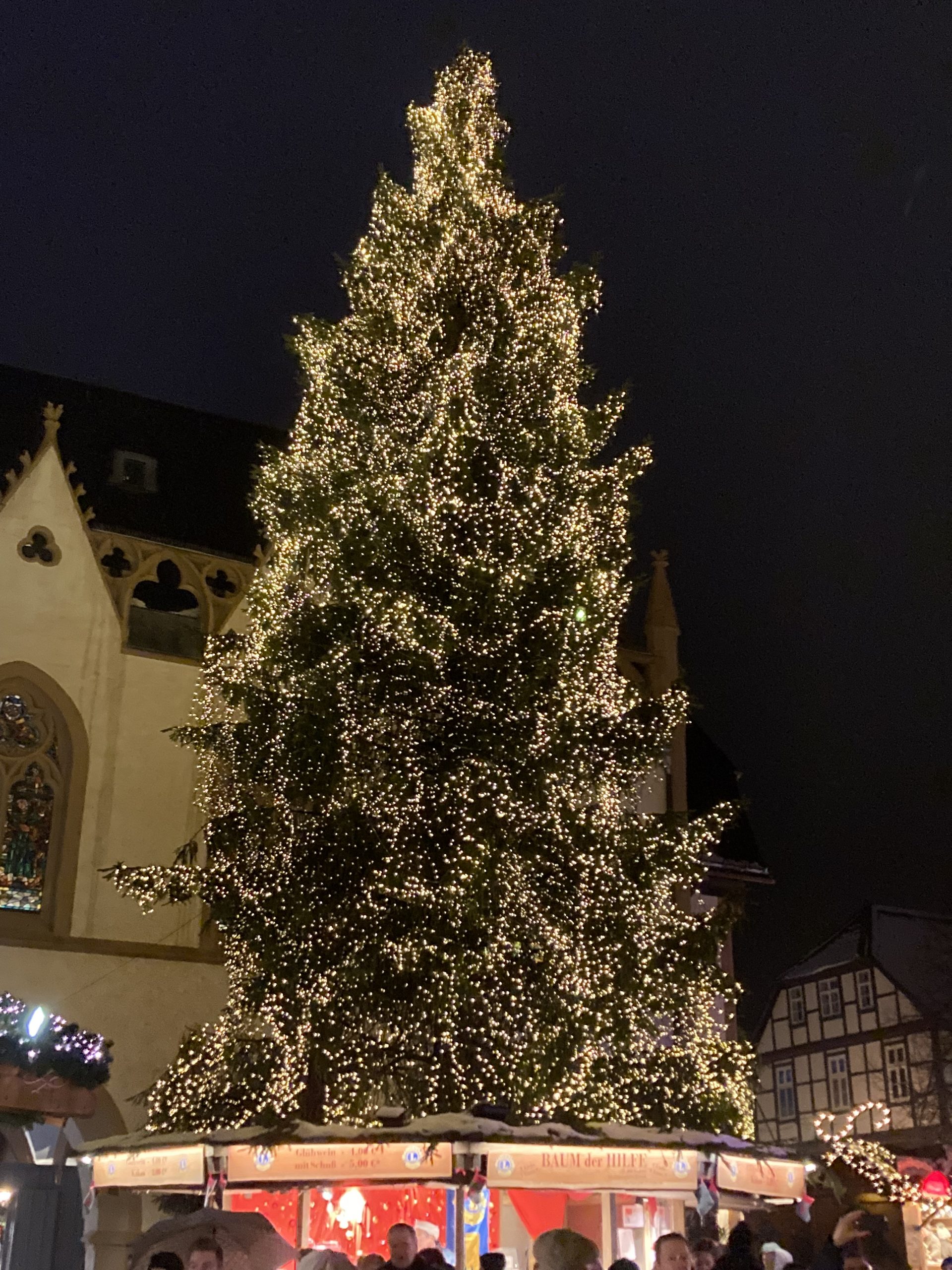 Ein großer Weihnachtsbaum, geschmückt mit funkelnden Lichtern und farbenfrohen Ornamenten, steht stolz in der Mitte eines belebten Stadtplatzes und verbreitet Weihnachtsstimmung bei allen Vorbeikommenden.